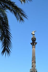 Low angle view of bird perching on statue against clear blue sky