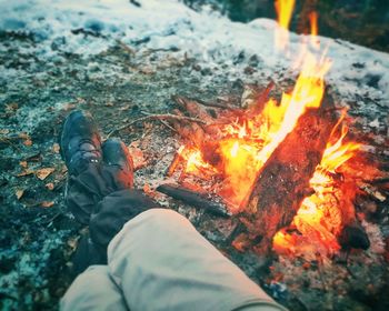 Low section of person sitting by campfire during winter