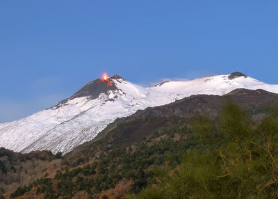 Low angle view of snowcapped volcano erupting against blue sky