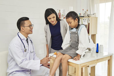 Doctor examining girl sitting by mother at hospital