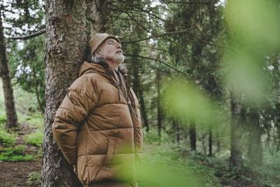 Senior man wearing jacket standing by tree in forest