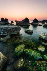 Rocks at seashore against sky during sunset