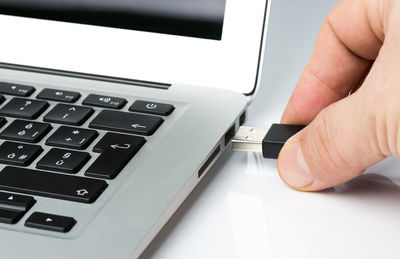 Cropped hand putting usb stick in laptop at table