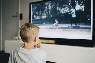Rear view of boy watching smart tv in living room at home