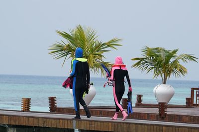 Full length of friends wearing diving suits while walking on pier