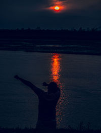 Rear view of man standing by river during sunset