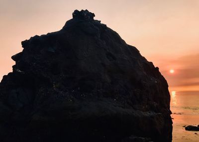 Low angle view of rock formation on sea against sky during sunset