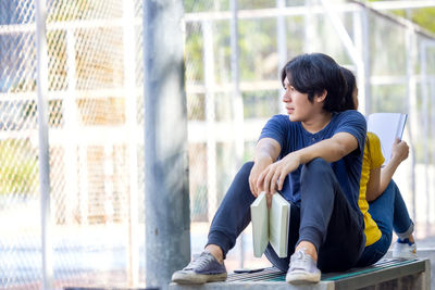 When sitting on a park bench, a pretty smiling young asian woman looks at her boyfriend's book