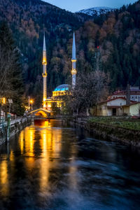 Illuminated bridge over river by buildings in city at night