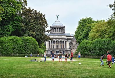 Group of people playing football in a park in front of building