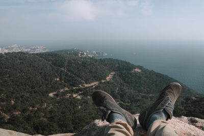 Low section of person relaxing on mountain by sea against sky