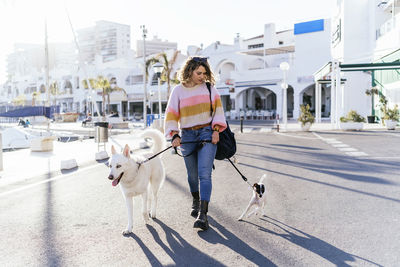 Woman amidst siberian husky and jack russell terrier walking on road in city