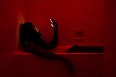 Side view of mid adult man sitting in bathtub while using mobile phone