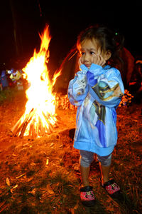 Cute girl with hand on chin standing against campfire on field at night