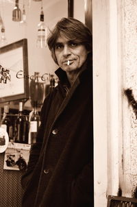 Portrait of mature man smoking cigarette while standing against store