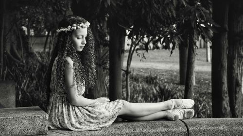 Side view of girl with curly hair sitting on retaining wall in park