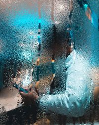 Side view of person using phone seen through wet window