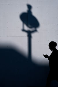 Silhouette person  with phone standing against wall