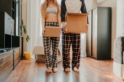 Low section of couple holding boxes while standing on floor at home