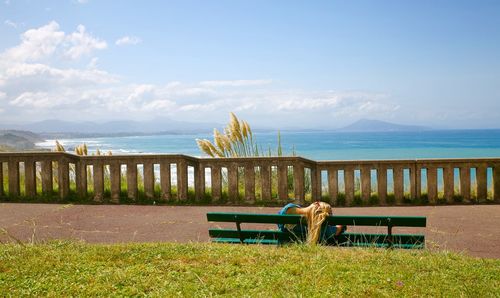 People sitting on bench by sea against sky