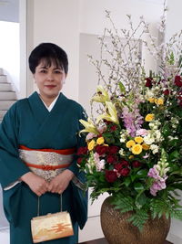 Portrait of woman standing by potted plant