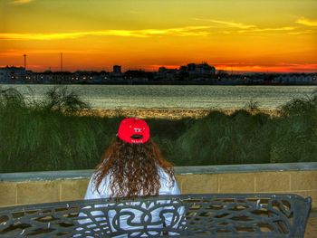 Portrait of red railing by river against sky during sunset