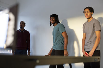 Friends standing by wall while playing table tennis in games room