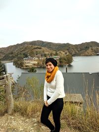 Portrait of smiling young woman standing by lake against sky