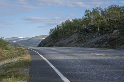 Empty road by trees against sky