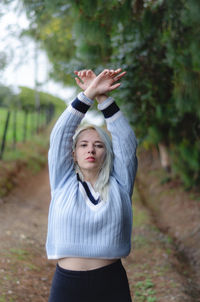 Portrait of woman with arms raised standing on footpath 