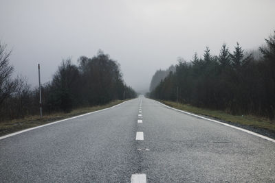 Empty road amidst trees against clear sky