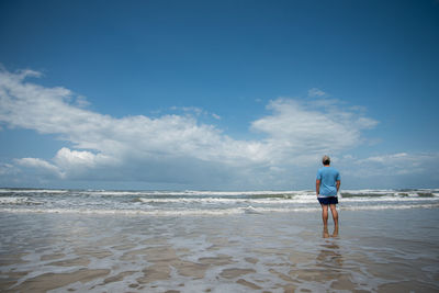 Rear view of man standing at beach against sky