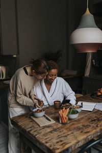 Non-binary couple sharing smart phone while having breakfast at home