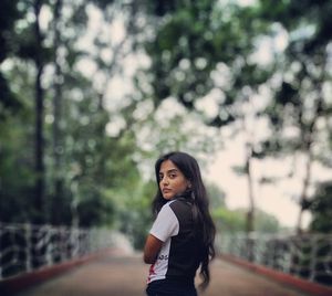 Portrait of young woman standing against trees