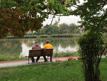 Rear view of people sitting on bench at lakeshore