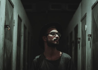 Thoughtful young man standing amidst lockers in corridor