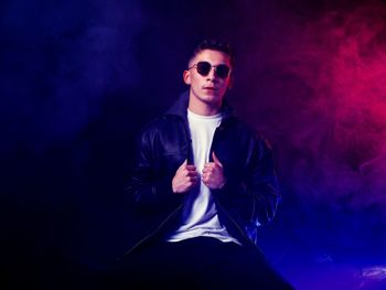 Young man wearing sunglasses while standing against black studio background 