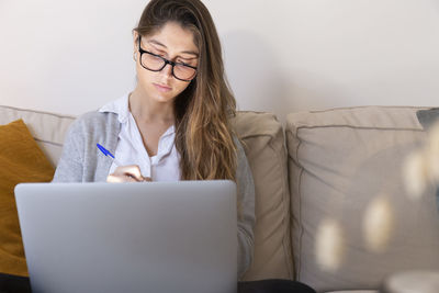 Young woman wearing eyeglasses studying on laptop at home