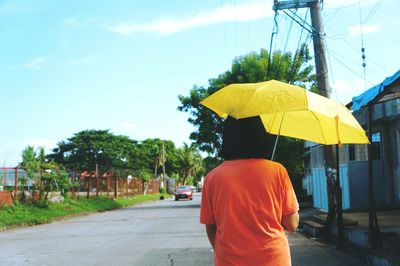 Rear view of woman with umbrella walking on road against sky