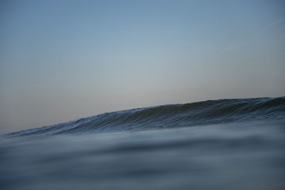 Waves splashing in sea against sky at sunset