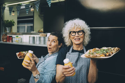 Portrait of senior owner with assistant holding street food in city