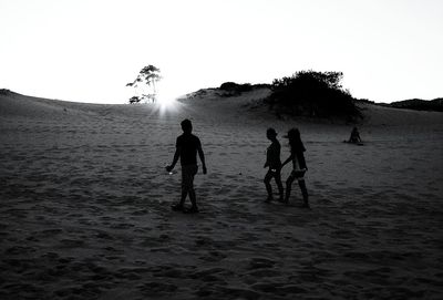Silhouette friends walking at beach against clear sky