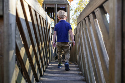Rear view of boy walking on wooden footbridge