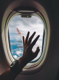 Cropped image of hand against sky seen through airplane window