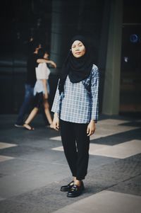 Full length portrait of woman standing on footpath in city