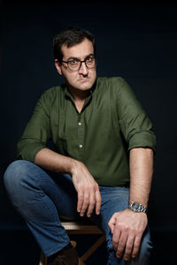 Full length portrait of man sitting against black background