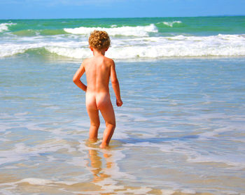 Rear view of shirtless boy standing in sea