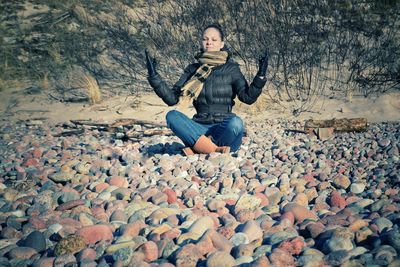Woman meditating while sitting on pebbles during winter