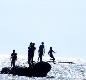 Silhouette people enjoying at sea shore against clear sky