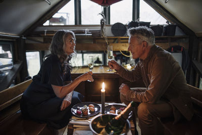 Senior couple having a candlelight dinner on a boat in boathouse clinking champagne glasses